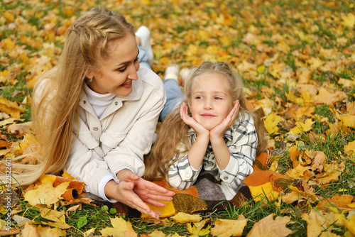The Caucasian family has fun in the park. The girl and mother lie on a blanket. Mother looks at her daughter and smiles