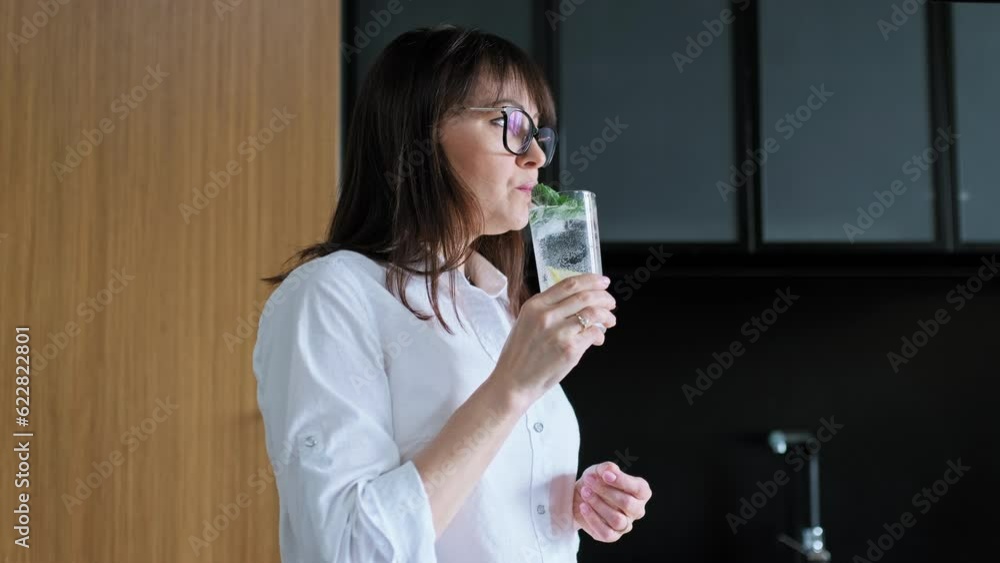 Mature woman drinking glass of water with lemon ice mint Mature woman drinking glass of water with lemon ice mint