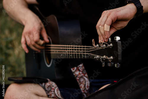 Hands  strings  guitar. The musician tunes the instrument. Black acoustic guitar. Summer  evening  music.
