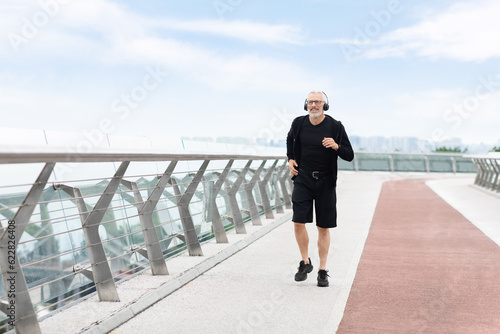 Happy elderly man jogging outside by bridge, copy space