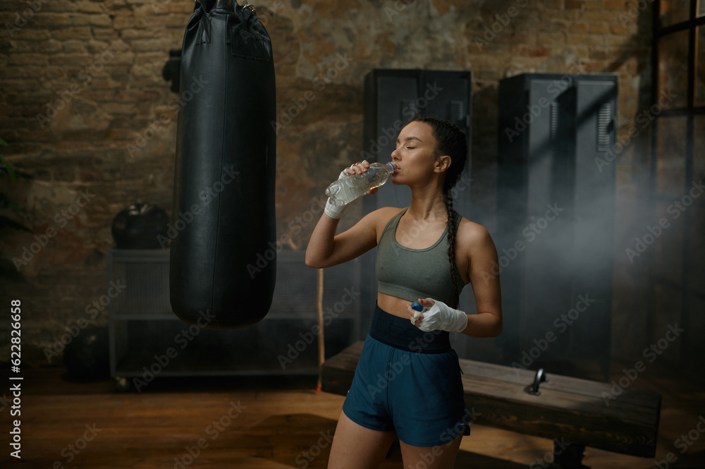 Woman boxer drinking water from plastic bottle quenching thirst after exercise