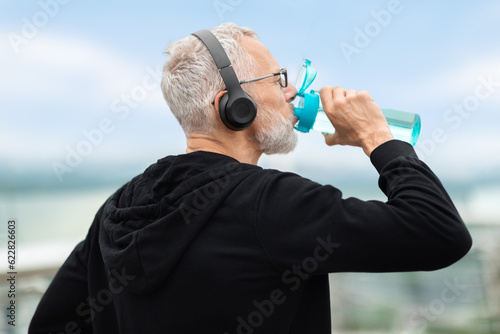 Closeup of elderly sportsman drinking water during workout outdoors