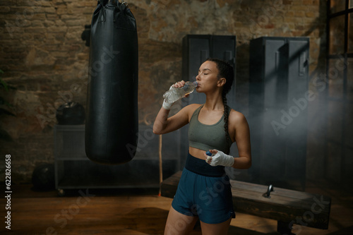 Woman boxer drinking water from plastic bottle quenching thirst after exercise