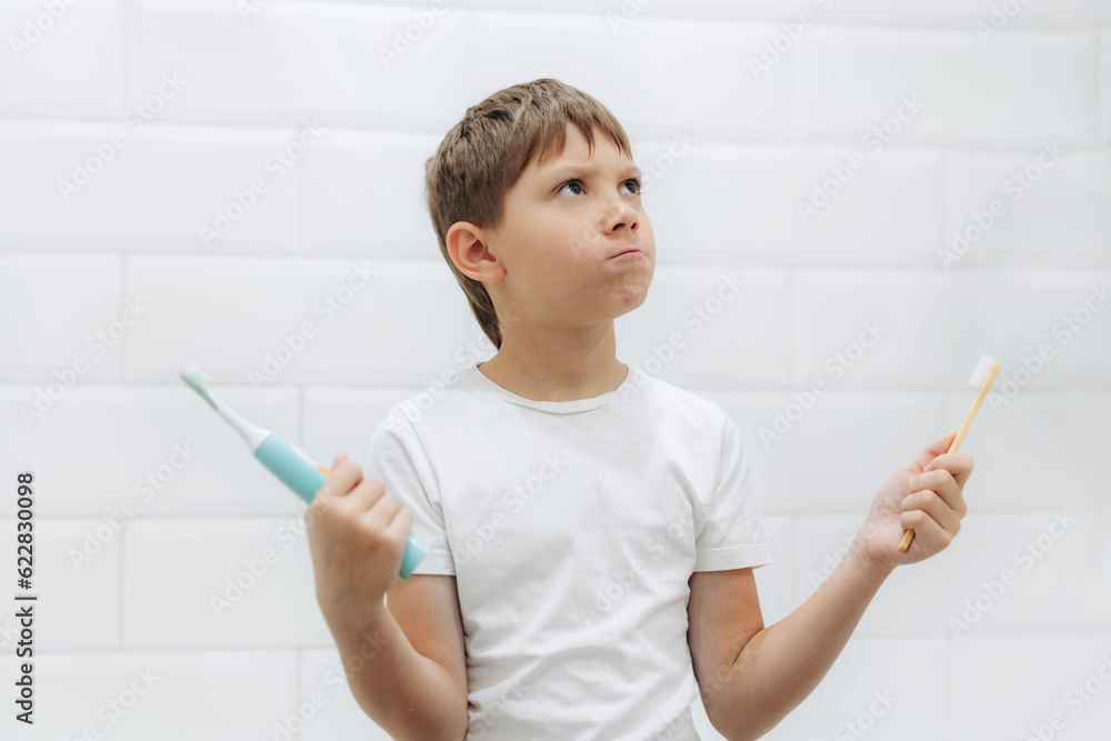 cute 8 years old boy holding bamboo and electric tooth brush making choice cute 8 years old boy holding bamboo and electric tooth brush making choice