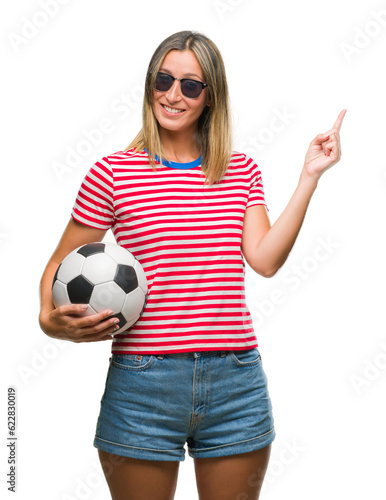 Young beautiful woman holding soccer football ball over isolated background very happy pointing with hand and finger to the side