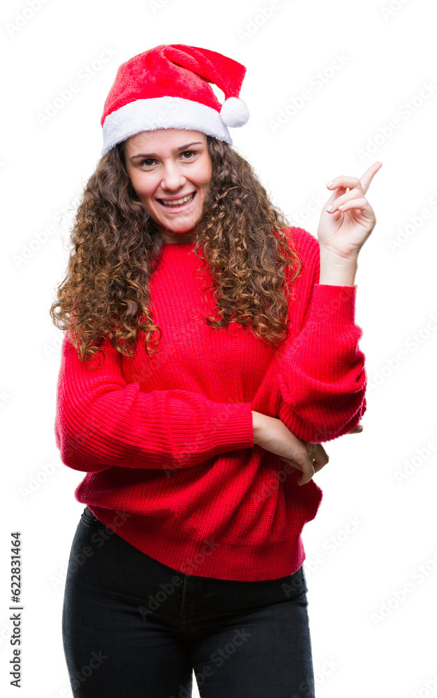 Young brunette girl wearing christmas hat over isolated background with a big smile on face, pointing with hand and finger to the side looking at the camera. Young brunette girl wearing christmas hat over isolated background with a big smile on face, pointing with hand and finger to the side looking at the camera.