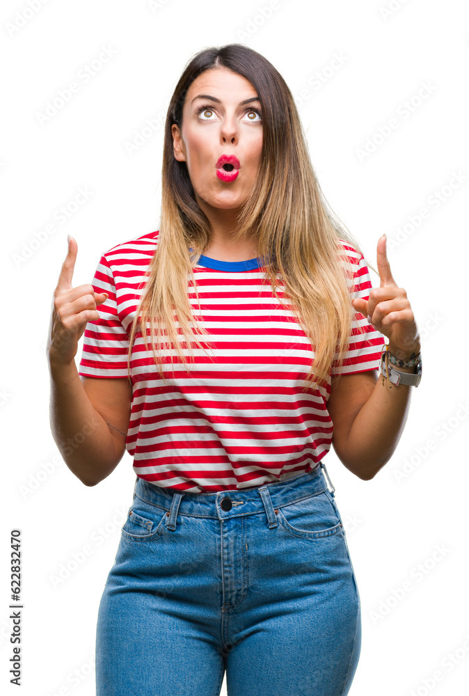 Young beautiful woman casual look over isolated background amazed and surprised looking up and pointing with fingers and raised arms. Young beautiful woman casual look over isolated background amazed and surprised looking up and pointing with fingers and raised arms.
