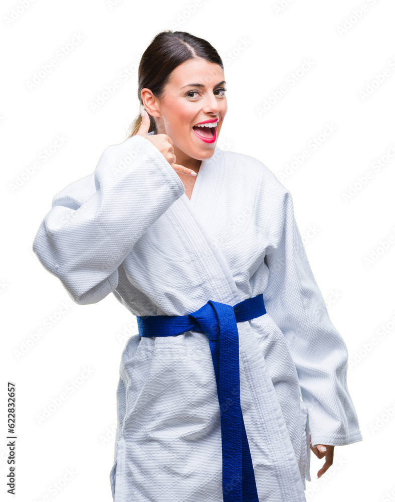 Young beautiful woman wearing karate kimono uniform over isolated background smiling doing phone gesture with hand and fingers like talking on the telephone. Communicating concepts. Young beautiful woman wearing karate kimono uniform over isolated background smiling doing phone gesture with hand and fingers like talking on the telephone. Communicating concepts.