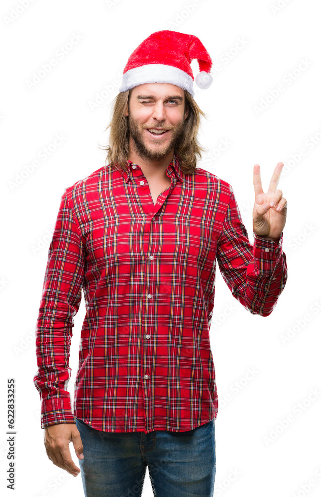 Young handsome man with long hair wearing santa claus hat over isolated background smiling with happy face winking at the camera doing victory sign. Number two. Young handsome man with long hair wearing santa claus hat over isolated background smiling with happy face winking at the camera doing victory sign. Number two.