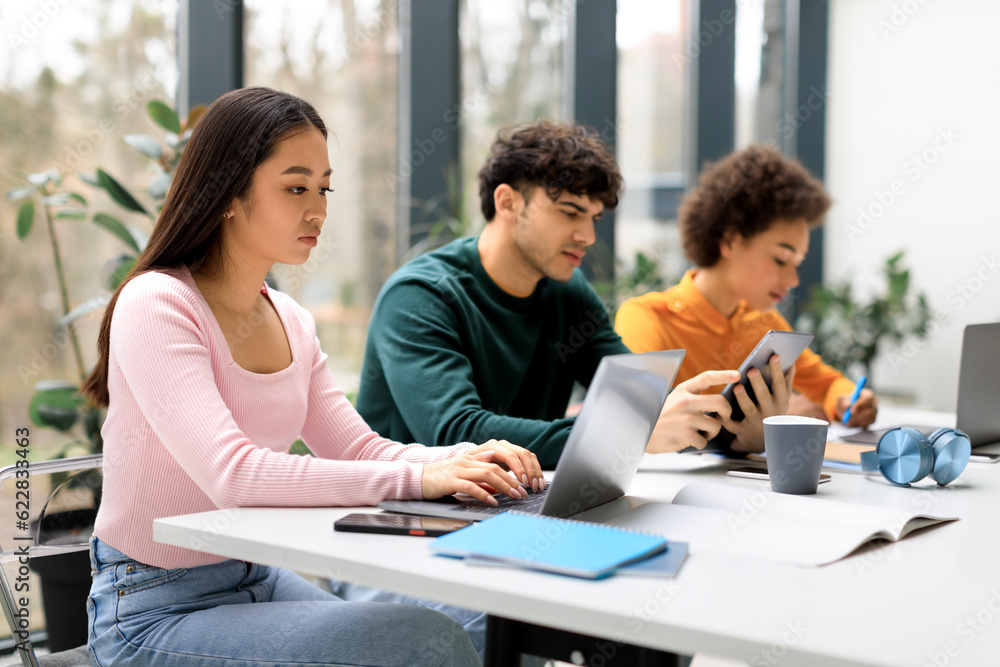 Group of diverse students studying for test, making project or homework together, focus on asian lady using laptop
