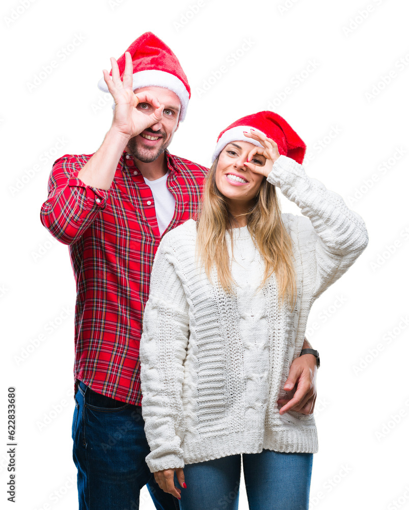 Young couple in love wearing christmas hat over isolated background doing ok gesture with hand smiling, eye looking through fingers with happy face. Young couple in love wearing christmas hat over isolated background doing ok gesture with hand smiling, eye looking through fingers with happy face.