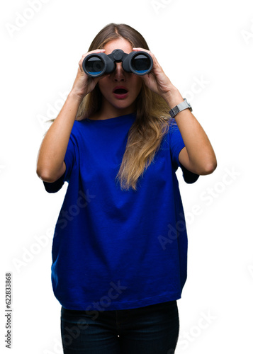Young beautiful blonde woman looking through binoculars over isolated background scared in shock with a surprise face, afraid and excited with fear expression