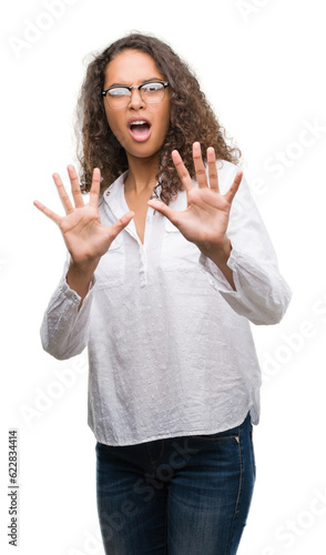 Beautiful young hispanic woman afraid and terrified with fear expression stop gesture with hands, shouting in shock. Panic concept.