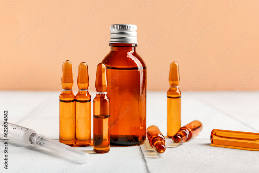 Medical ampules, bottle and syringe on white tile table