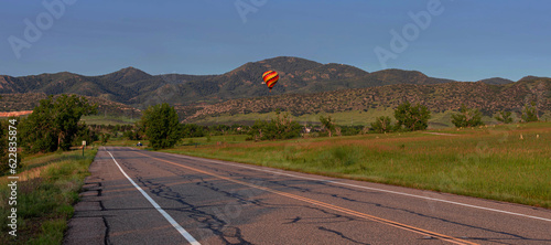 Hot air balloon rising above trees with rocky mountains in back ground and clear blue morning sky. in Jefferson county, Colorado photo