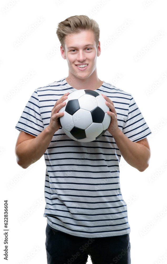 Young handsome blond man holding soccer ball with a happy face standing and smiling with a confident smile showing teeth