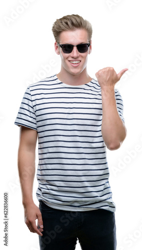 Young handsome blond man wearing sunglasess pointing with hand and finger up with happy face smiling