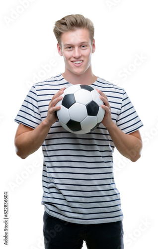 Young handsome blond man holding soccer ball with a happy face standing and smiling with a confident smile showing teeth