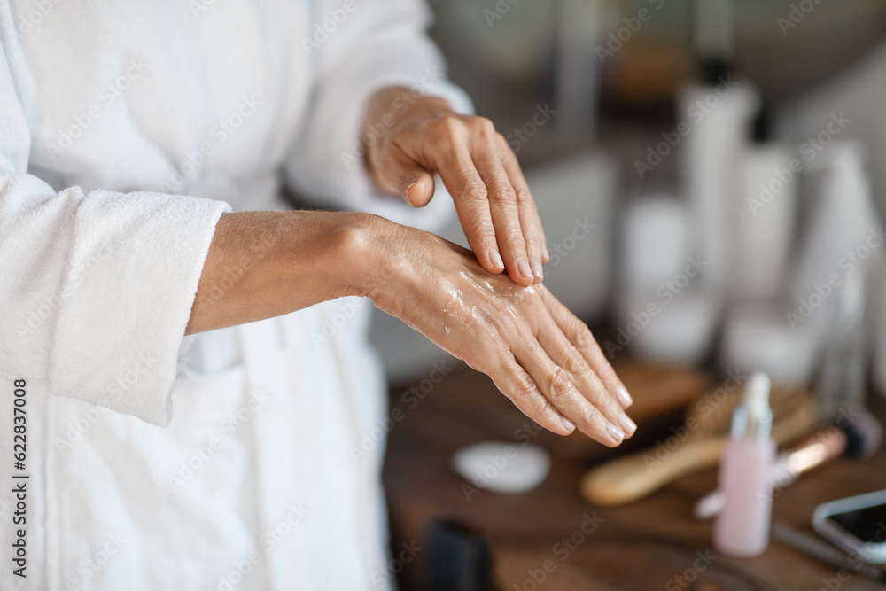 Dry Skin Treatments. Mature woman applying anti-aging serum on hands at home