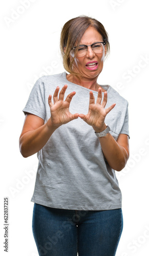 Middle age senior hispanic woman wearing glasses over isolated background disgusted expression, displeased and fearful doing disgust face because aversion reaction. With hands raised