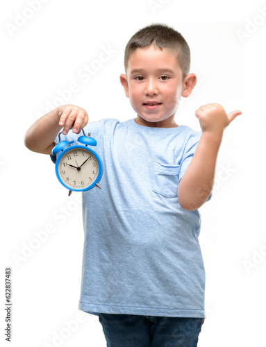 Little child holding alarm clock pointing with hand and finger up with happy face smiling