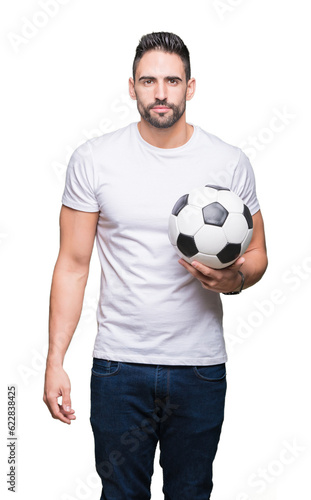 Young man holding soccer football ball over isolated background with a confident expression on smart face thinking serious
