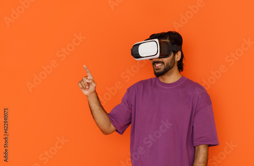 Young man using virtual reality headset. Isolated on orange background