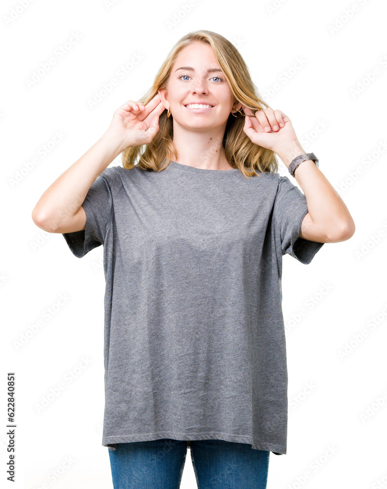 Fototapeta premium Beautiful young woman wearing oversize casual t-shirt over isolated background Smiling pulling ears with fingers, funny gesture. Audition problem