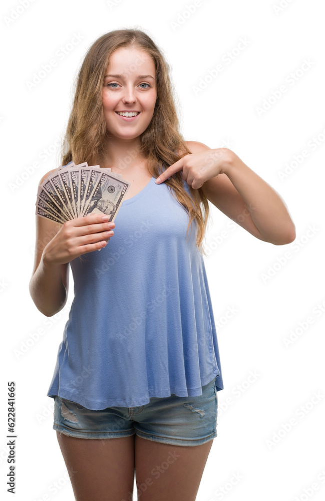 Young blonde woman holding dollars with surprise face pointing finger to himself Young blonde woman holding dollars with surprise face pointing finger to himself