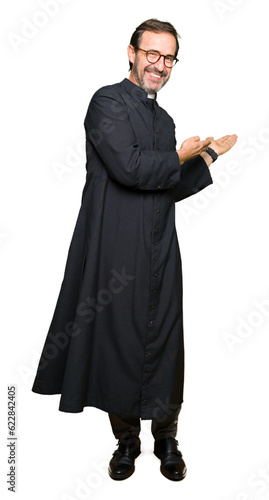 Middle age priest man wearing catholic robe Inviting to enter smiling natural with open hand