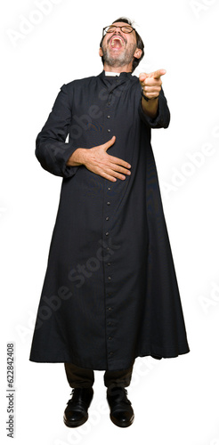 Middle age priest man wearing catholic robe Laughing of you, pointing to the camera with finger hand over chest, shame expression
