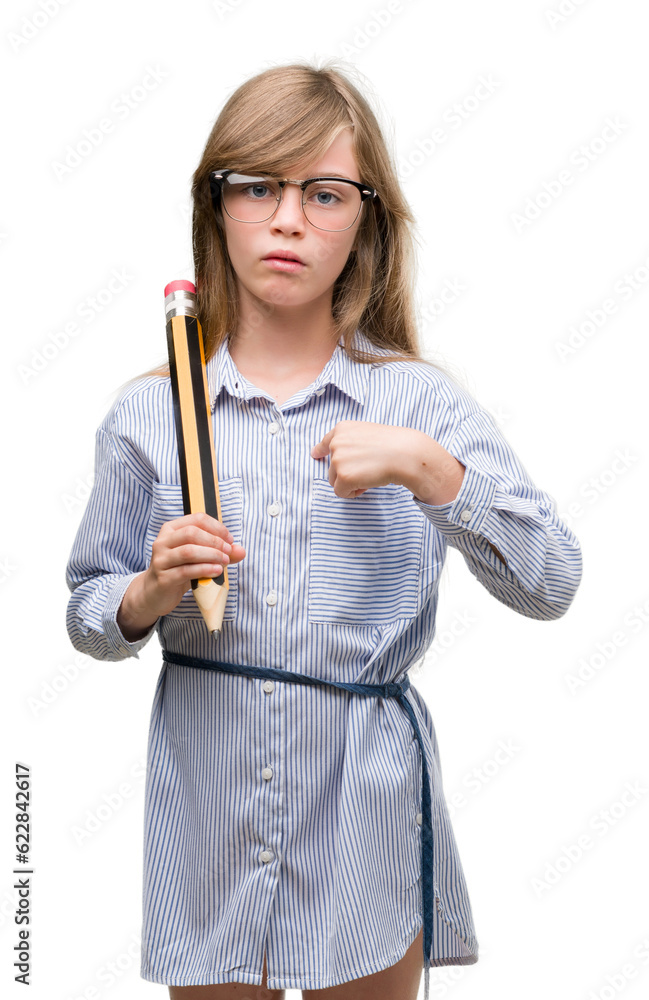 Young blonde child holding big pencil with surprise face pointing finger to himself Young blonde child holding big pencil with surprise face pointing finger to himself