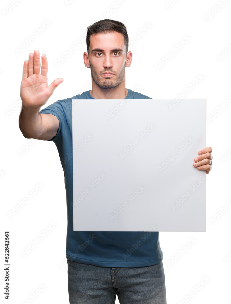 Handsome young man holding advertising banner with open hand doing stop sign with serious and confident expression, defense gesture Handsome young man holding advertising banner with open hand doing stop sign with serious and confident expression, defense gesture