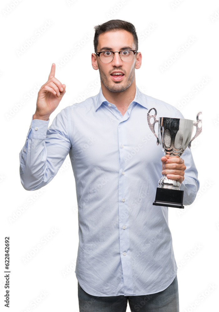 Handsome young man holding trophy surprised with an idea or question pointing finger with happy face, number one Handsome young man holding trophy surprised with an idea or question pointing finger with happy face, number one