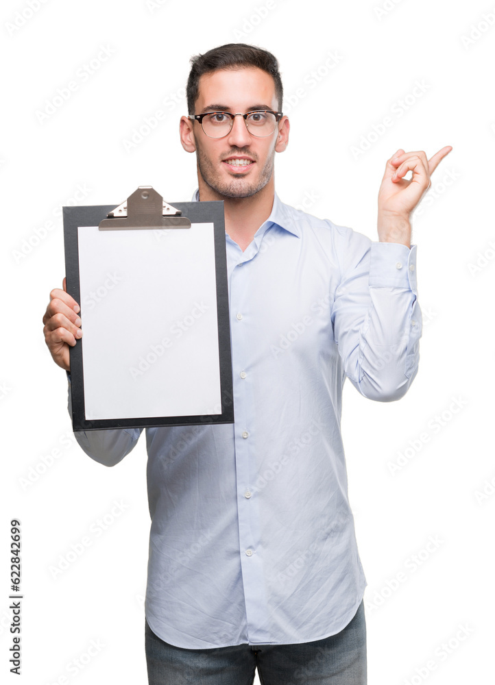 Handsome young business man showing a clipboard very happy pointing with hand and finger to the side Handsome young business man showing a clipboard very happy pointing with hand and finger to the side