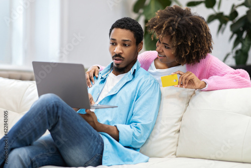 Loving black spouses shopping from home, using laptop, bank card