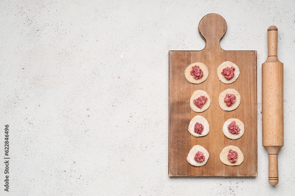 Wooden board of raw dough with minced meat for preparing dumplings on light background Wooden board of raw dough with minced meat for preparing dumplings on light background