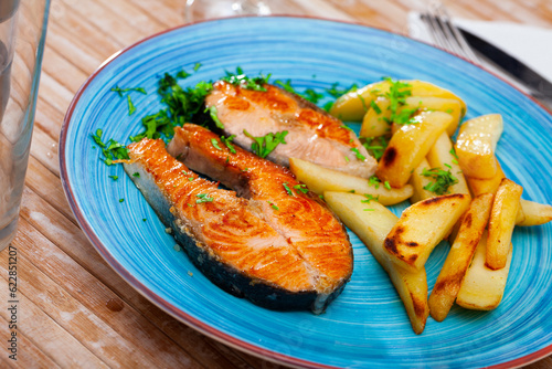 Roasted salmon steaks garnished with fried potatoes served with fresh greens..