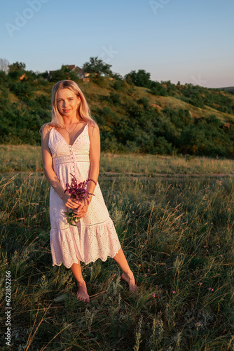 Elegant young woman with wildflowers on nature background in summer at sunset. female is relaxing in the field with flowers. Soft golden color