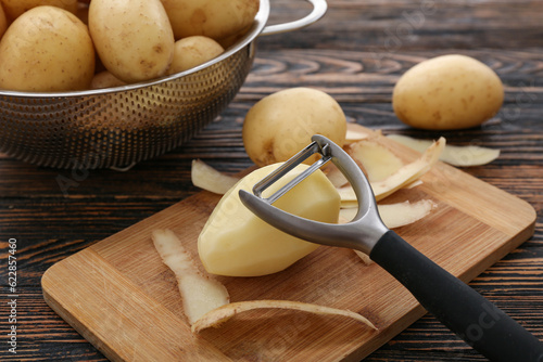Board and colander with raw potatoes on wooden background