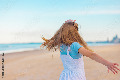 View from behind of young girl in dress twirling on the the beach