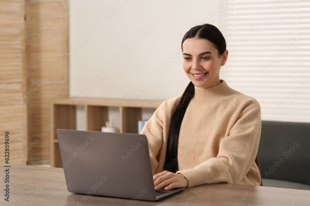 Happy woman working with laptop at wooden desk in room Happy woman working with laptop at wooden desk in room