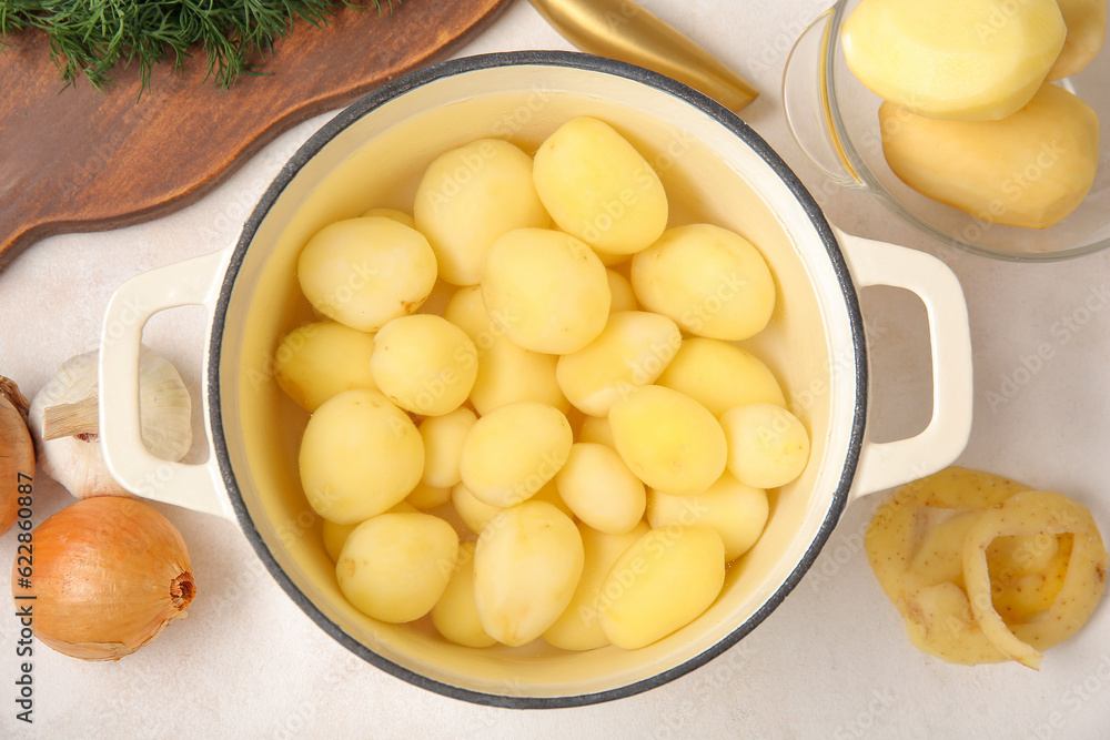 Pot with peeled potatoes on light background