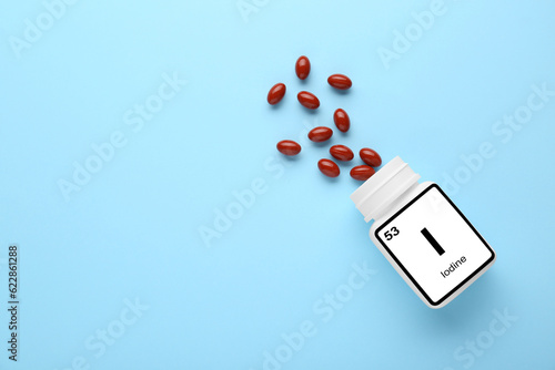 Plastic jar and iodine pills on light blue background, flat lay. Space for text photo