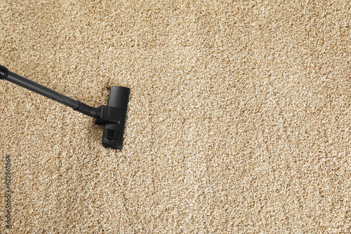 Removing dirt from beige carpet with modern vacuum cleaner, above view. Space for text © New Africa