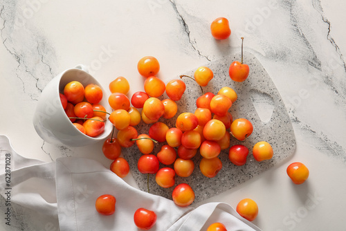 Board and cup with sweet yellow cherries on white background