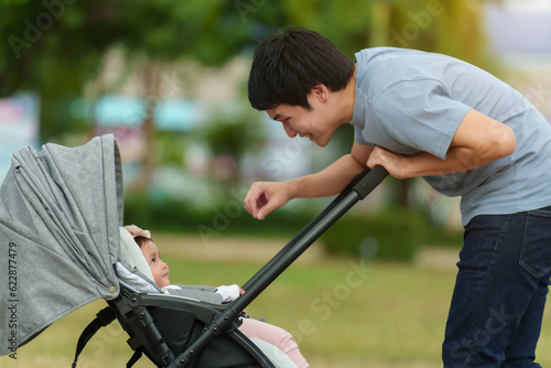 happy father talking and playing with her infant baby in the stroller while resting in park