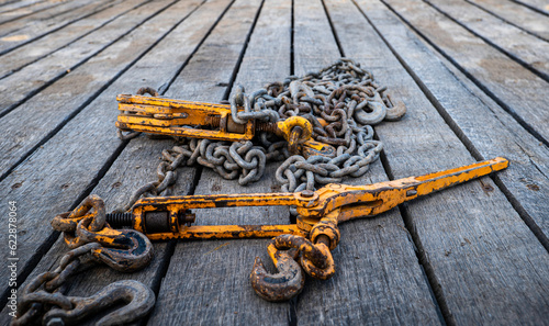 Obraz na płótnie Two old, used and rusty tie down chains and binders, used to secure an object in place on a flatbed trailer, when transporting cargo from place to place. w salonie