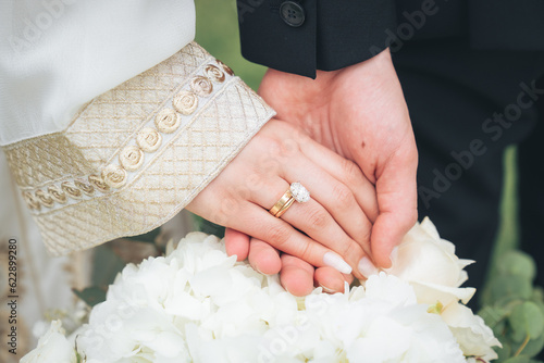 Close Up of Bride and Groom Holding Hands with Wedding Rings and White Flowers – Muslim Wedding, Marriage Ceremony, Love, Romance, Commitment, Engagement, Bridal Jewelry, Islamic Culture, Marriage