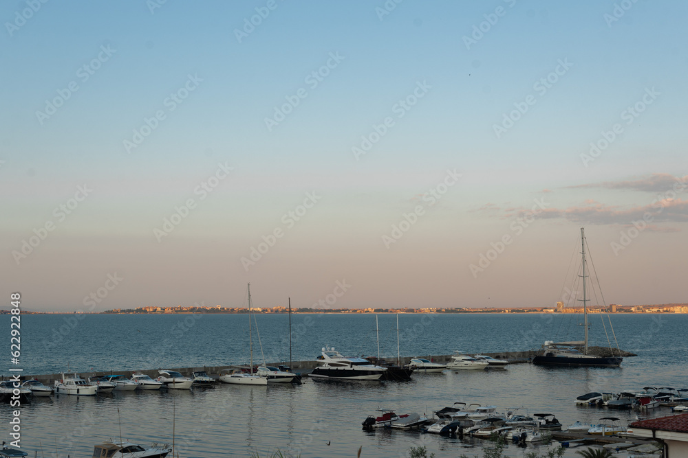 Boat on calm blue sea with sandy beach and clear sky at  dawn. Marina at sunrise